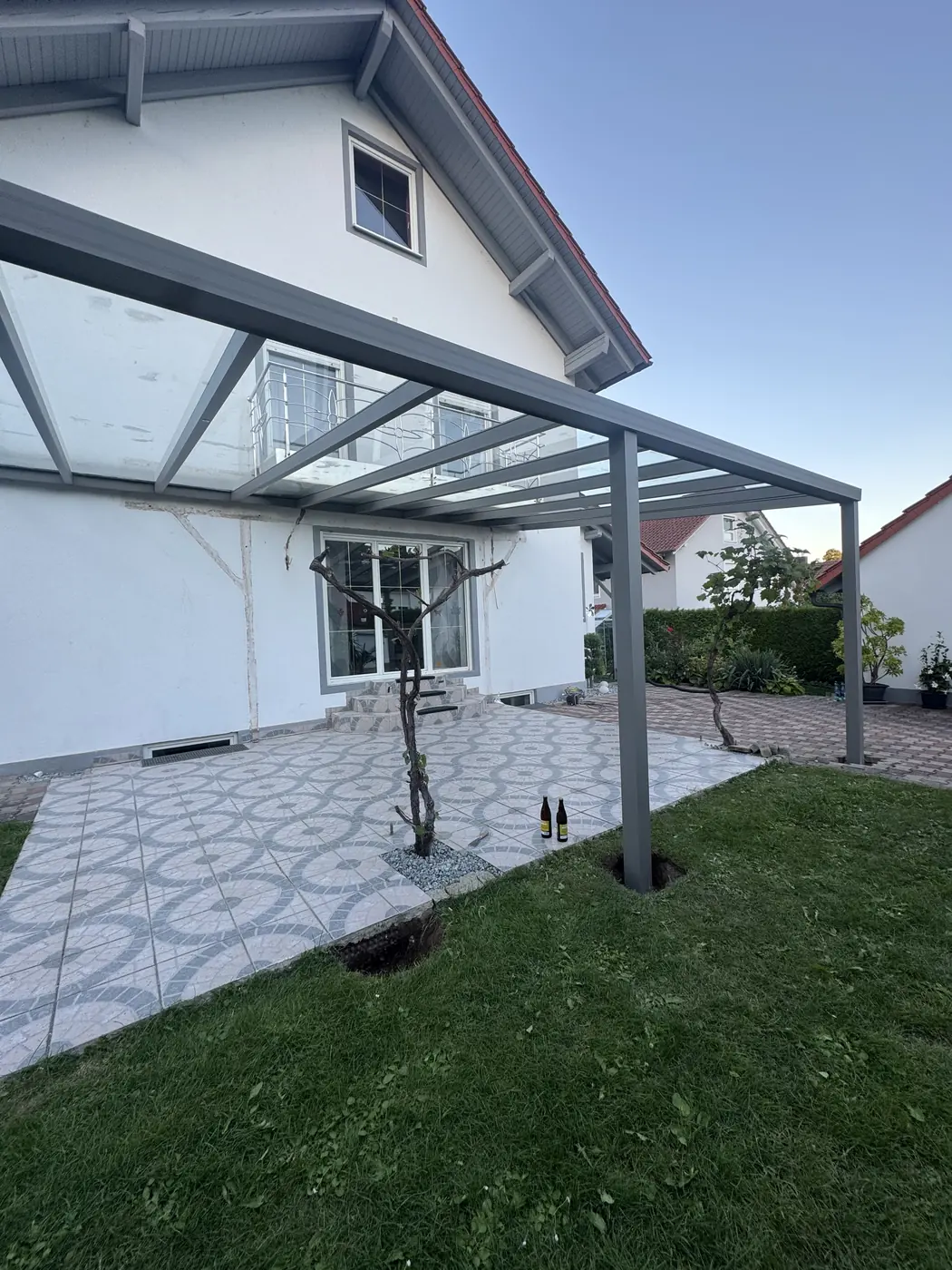 Terrassenüberdachung mit Glasdach über gefliester Terrasse